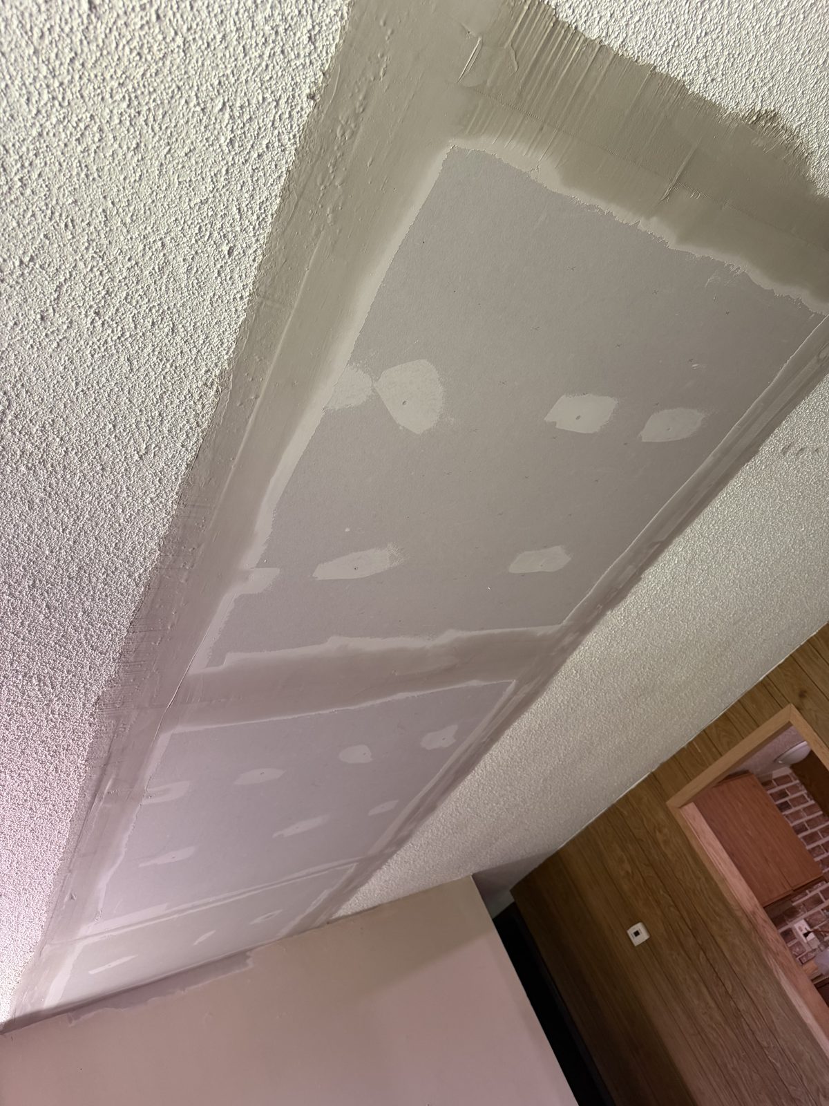 New drywall patch taped into a ceiling directly beside existing popcorn texture, ready for texture matching