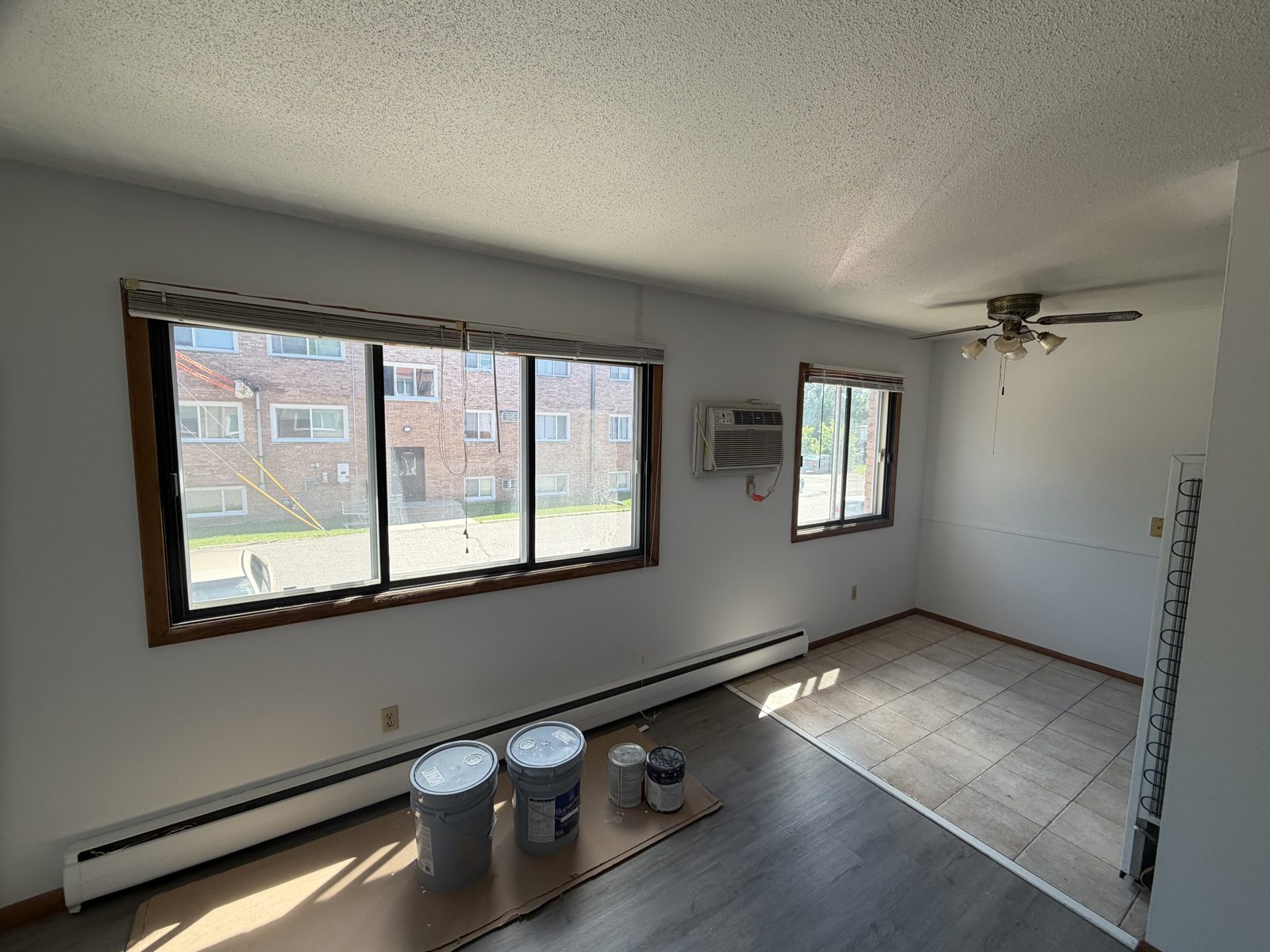 Empty apartment living room with freshly painted white walls, textured ceiling and paint buckets on the floor