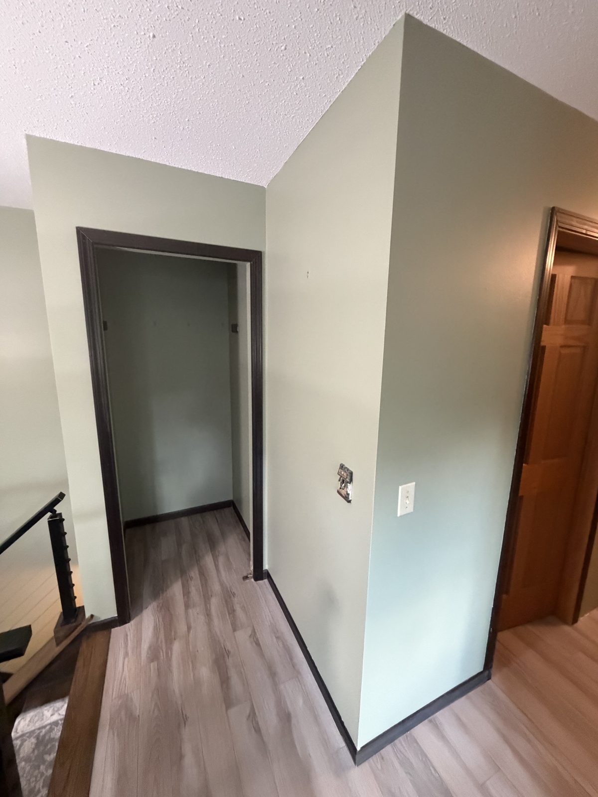 Stair landing with sage green walls cut in tight against dark stained door casing and baseboard