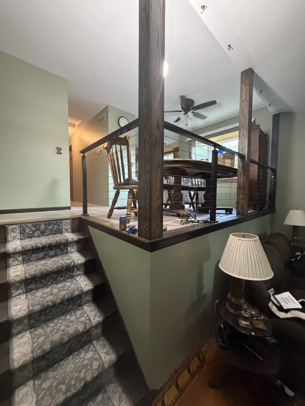Split-level stairwell with sage green walls freshly painted around a wood and cable stair railing