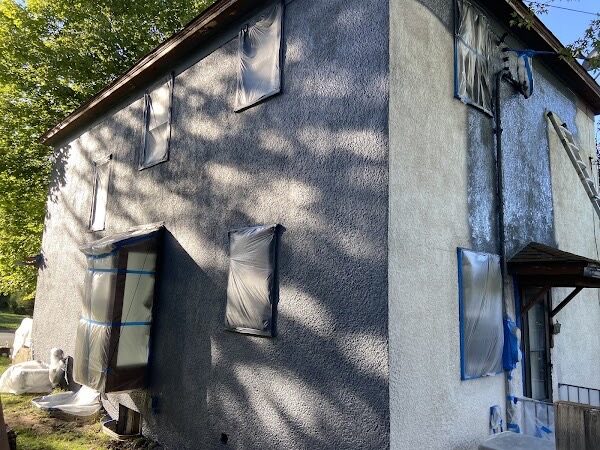 Two-story stucco home with every window and door masked in plastic and blue tape, primed and ready for exterior paint