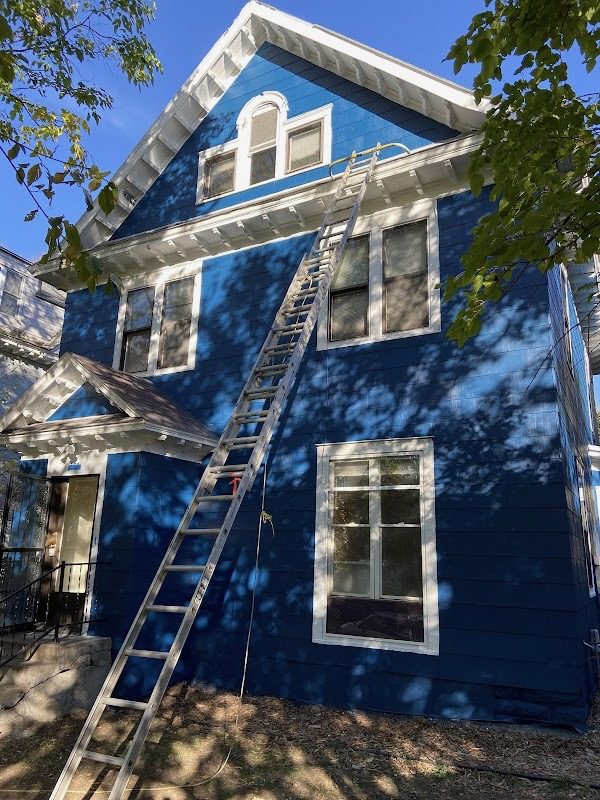 Side elevation of a navy blue repainted house with white trim, ladder in place during exterior painting