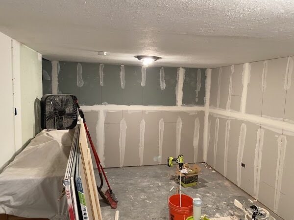 Finished basement walls with drywall hung and the first coat of joint compound applied over screws and seams