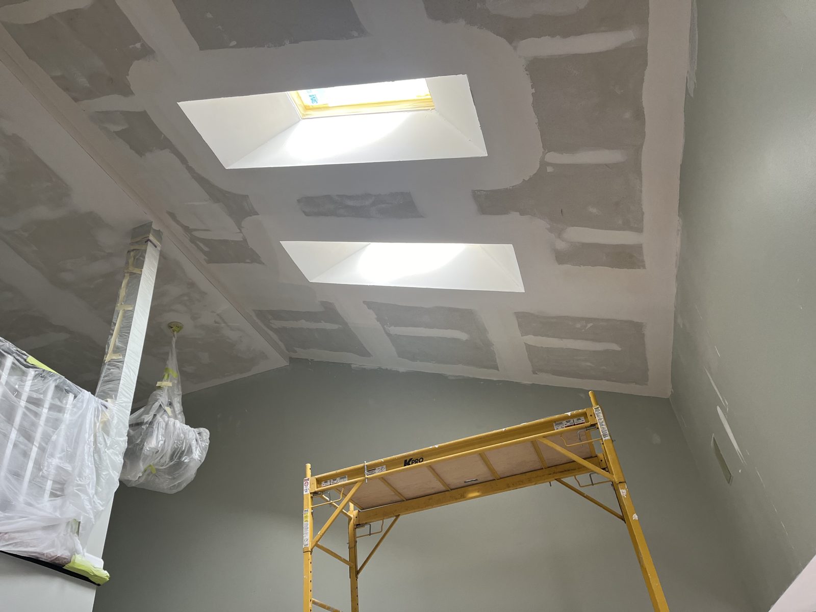 Vaulted ceiling under construction with two skylight light shafts drywalled and coated, scaffolding below