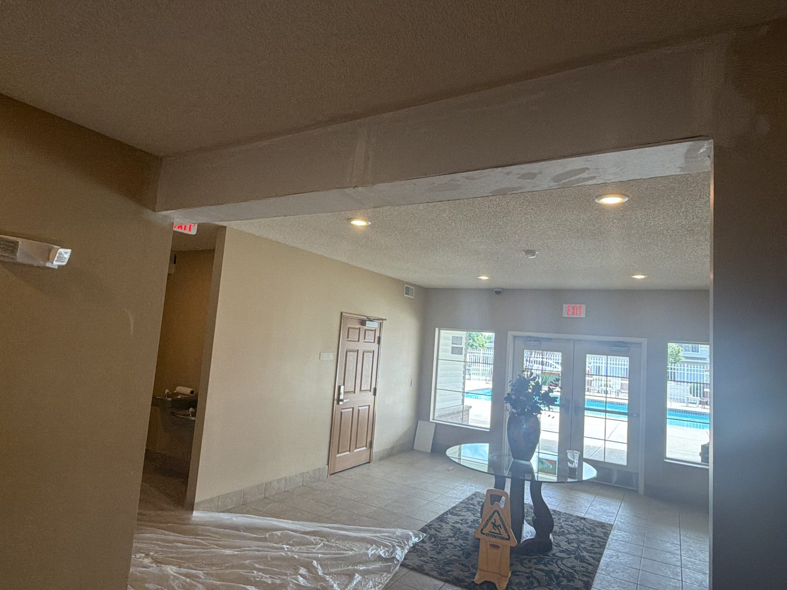 Hotel-style lobby entry with a drywall beam patched and coated, floors covered in plastic during the repair