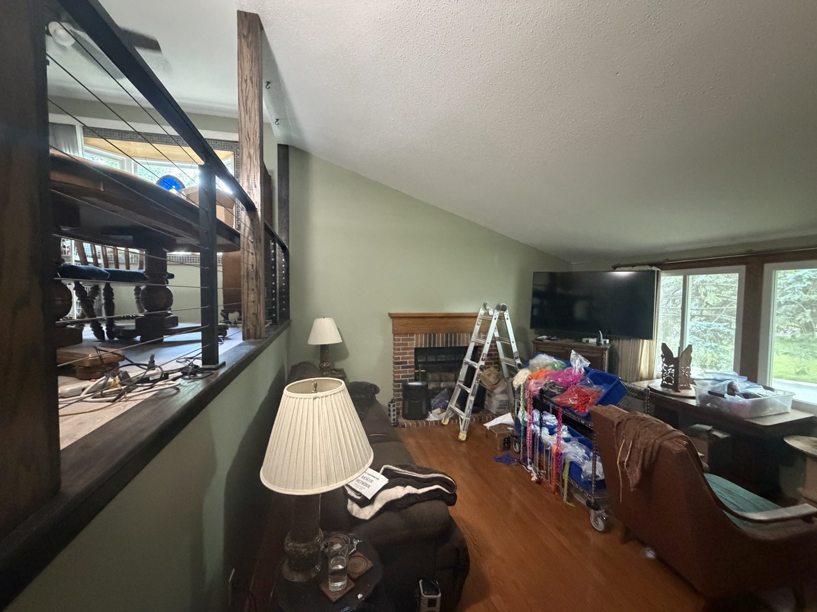 Living room with vaulted ceiling repainted white and walls in a soft sage green, brick fireplace and step ladder in place