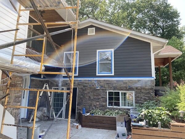 Home exterior mid-repaint with scaffolding set up, charcoal siding painted and windows masked off above a stone facade