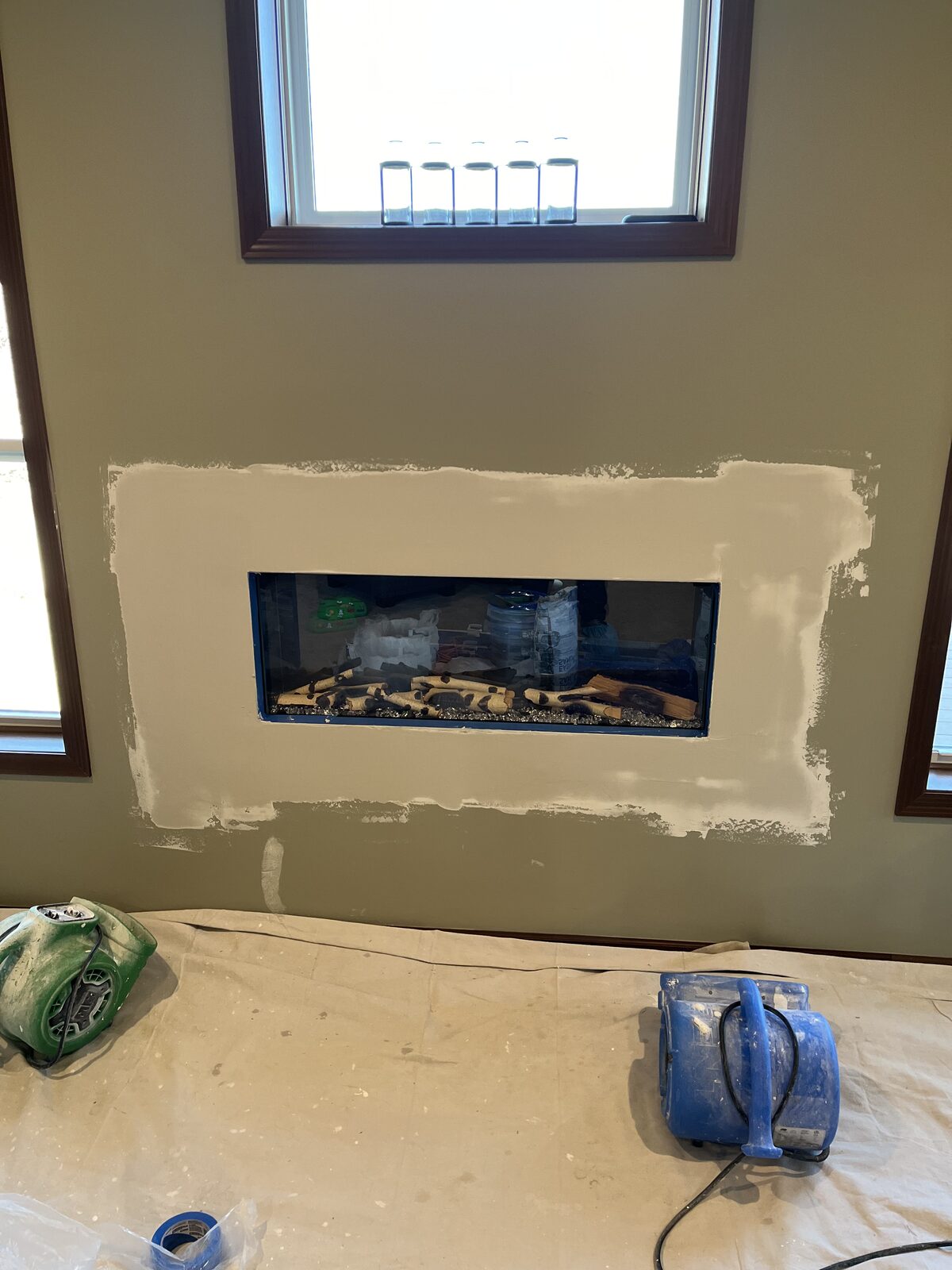 Wall around a linear gas fireplace patched with drywall compound and primed, floors covered with drop cloths