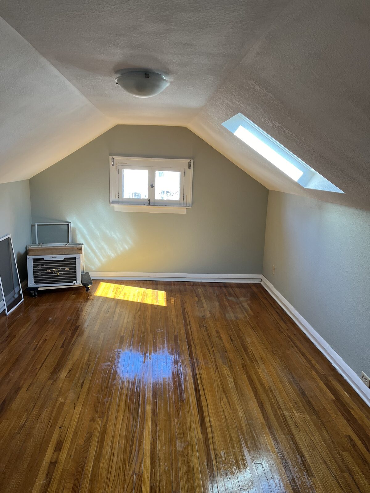 Finished attic bonus room with sage green painted walls, textured ceiling, skylight and hardwood floors