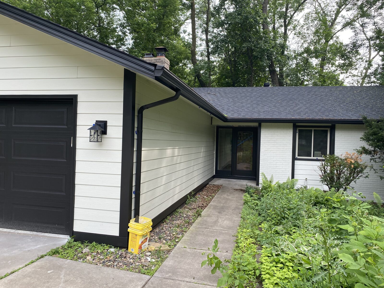 Garage and front entry of a home with freshly painted siding, painted brick and black trim