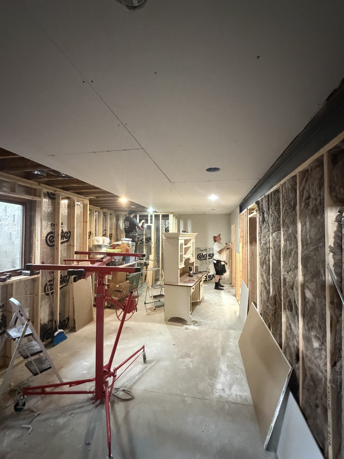 Basement under construction with the ceiling drywall hung and recessed lights cut in, open stud walls on both sides