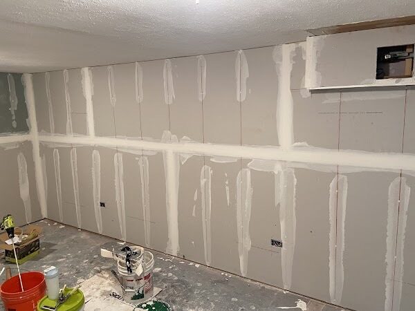 Long basement wall with drywall seams and butt joints coated in joint compound, ready for sanding