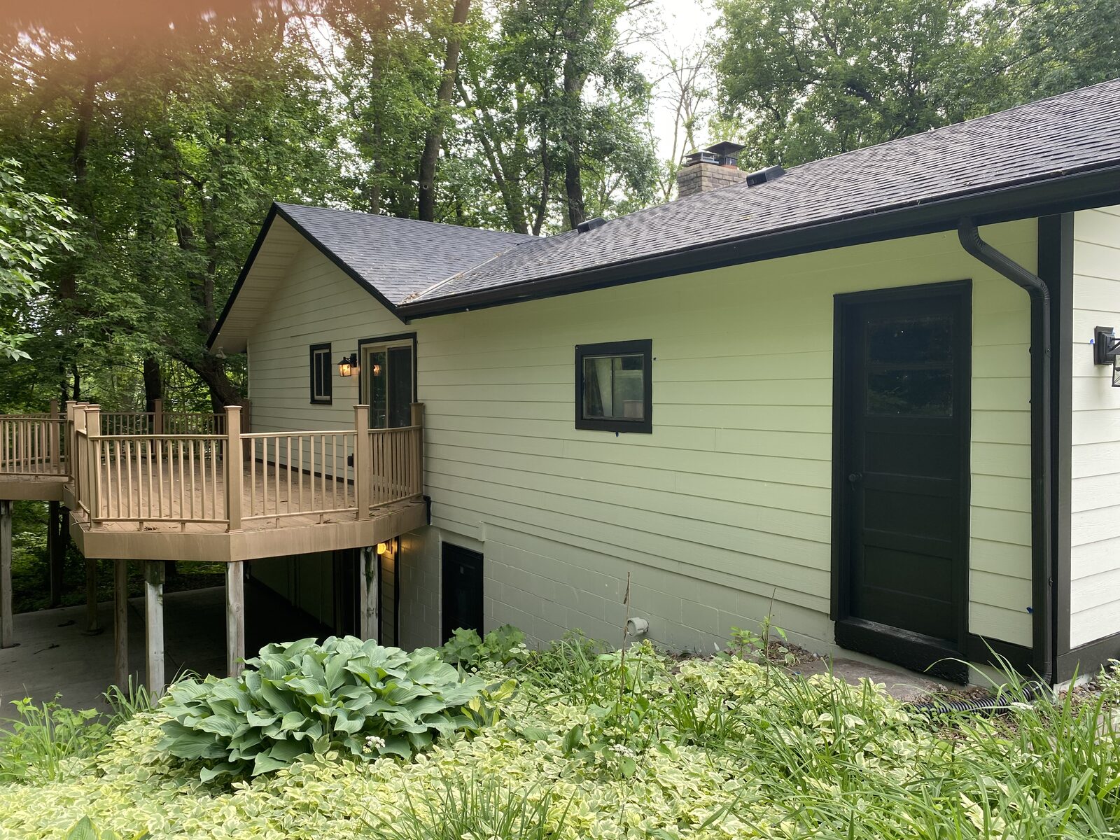 Side of a home painted sage green with black trim, elevated wood deck and painted block foundation